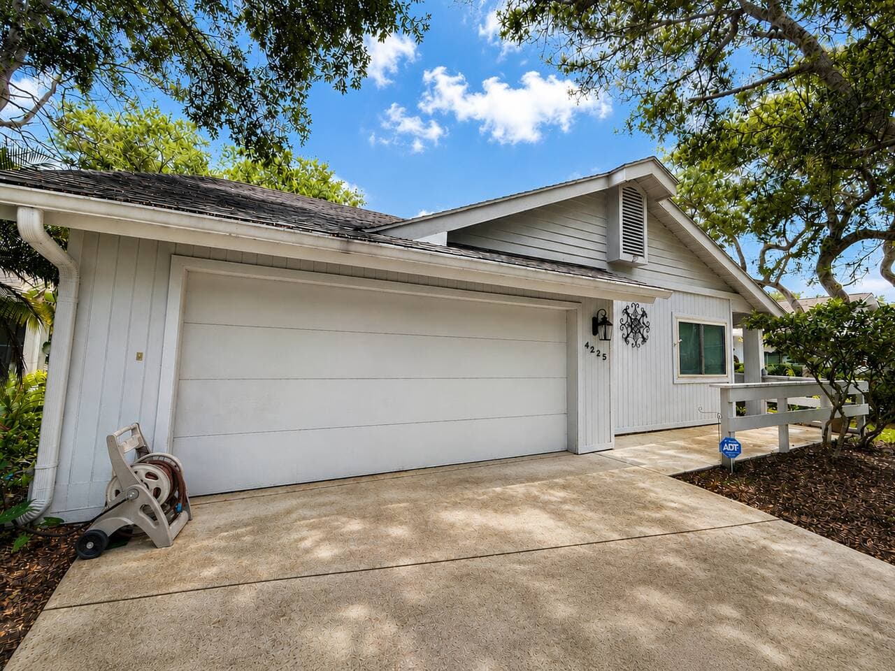 Front exterior of the single-story villa with attached two-car garage and oak-shaded driveway